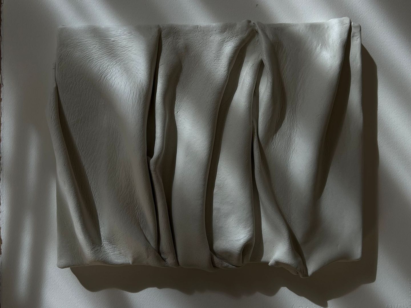 Wit reliëfkunstwerk met plooien en texturen aan een museumwand