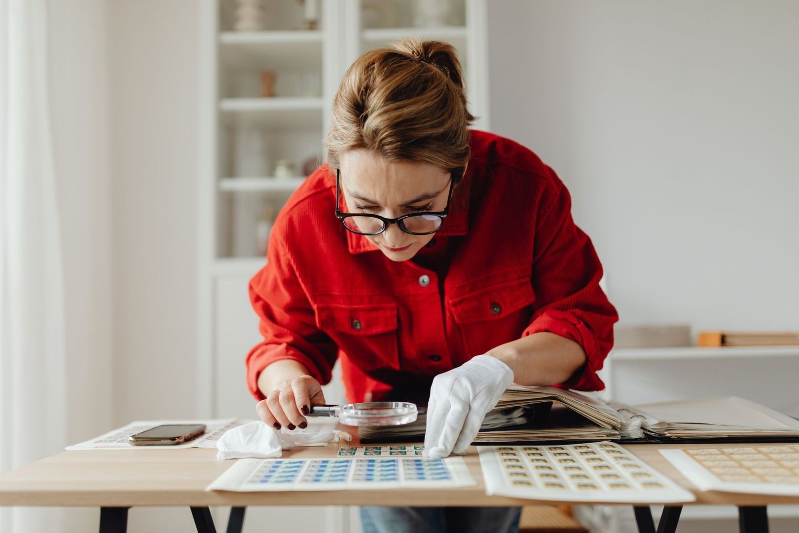 Onderzoeker bekijkt archiefmateriaal met een loep aan een tafel